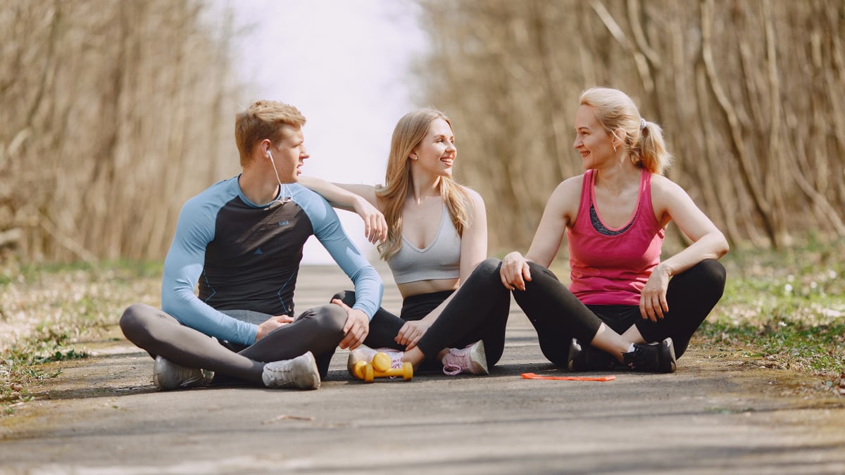 Three friends in sportswear sitting and conversing outdoors on a sunny day.